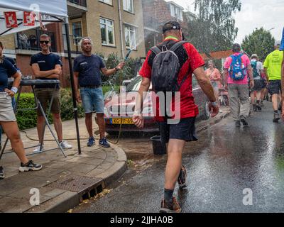 Un homme est vu jeter de l'eau aux marcheurs en raison des températures élevées pendant le plus grand événement de marche de plusieurs jours au monde. La marche des quatre jours (en néerlandais 'Vierdaagse') est considérée comme le premier exemple de l'esprit sportif et des liens internationaux entre militaires et civils de nombreux pays différents. Après deux ans d'annulation, il a été retenu à nouveau, mais le premier jour a été annulé en raison de températures chaudes, transformant les quatre marches en trois jours de marche. Il s'agit de l'édition 104 et le total officiel des marcheurs enregistrés était de 38 455 dans 69 pays. Ils peuvent choisir de marcher 30k Banque D'Images