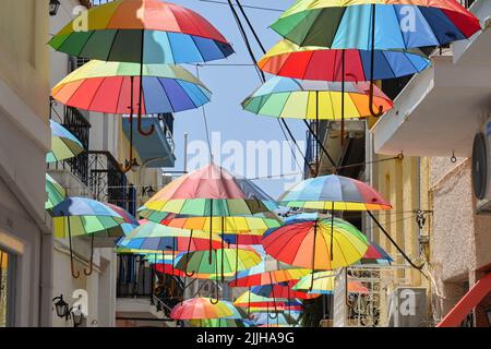 Aegina, Grèce - Mai 2022 : parasols colorés suspendus au-dessus d'une des rues étroites de la ville d'Aegina Banque D'Images