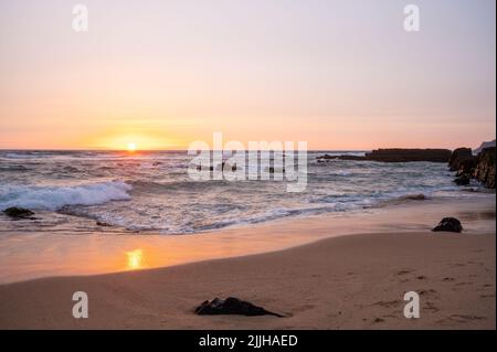 Sandy Cascais Beach au coucher du soleil avec des vagues qui s'écrasant sur quelques rochers Banque D'Images