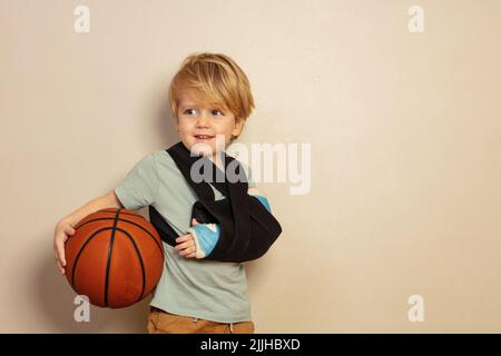 Joli garçon blond avec main cassée tenant le ballon de basket-ball Banque D'Images