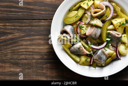 Vue rapprochée de la salade de hareng avec pommes de terre bouillies, concombres marinés et oignons rouges dans un bol sur fond de bois avec espace libre. Vue de dessus, fl Banque D'Images