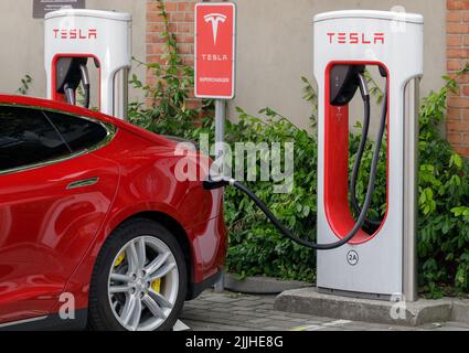 Poznan, Pologne. 26 juillet 2022 : une belle voiture électrique de tourisme rouge Tesla réapprovisionne sa batterie à une station de charge. Gros plan Banque D'Images