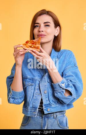 jeune femme avec tranche de pizza sur fond jaune. Banque D'Images