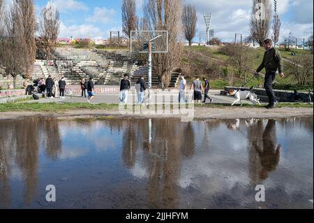 23.02.2022, Berlin, Allemagne, Europe - l'homme marche son chien et se reflète dans une flaque à Mauerpark à Prenzlauer Berg pendant que les jeunes hommes jouent au basket-ball. Banque D'Images