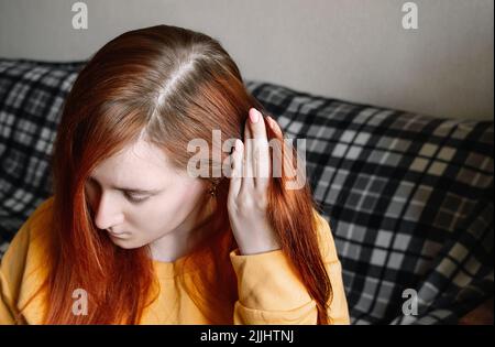 La jeune femme montre des racines de cheveux surcultivées. Concept d'auto-soin, coloration des cheveux à la maison. Premiers cheveux gris. Banque D'Images