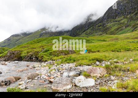 Glencoe scottish Highlands, modèle de randonneur femelle a libéré la marche près de la rivière avec le brouillard brumeux roulant sur les montagnes écossaises derrière, Ecosse, Royaume-Uni Banque D'Images