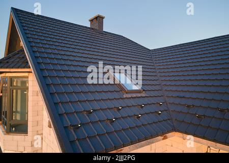 Gros plan de la fenêtre grenier sur le toit de la maison recouvert de bardeaux en céramique. Revêtement carrelé du bâtiment Banque D'Images