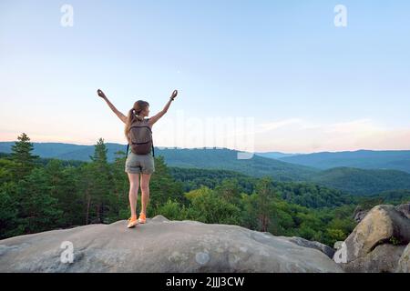 Une randonneur se tenant sur un sentier de randonnée en montagne levant les mains en profitant de la nature du soir pendant son voyage sur un sentier sauvage. Voyageur solitaire Banque D'Images