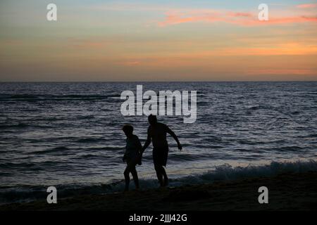 Silhouette d'un vieux couple qui marche contre les vagues spectaculaires de l'océan rouge au coucher du soleil avec une douce soirée mer sombre Banque D'Images