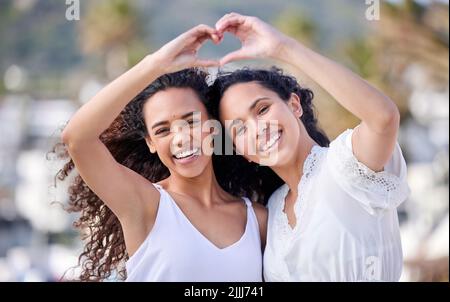 Mon meilleur ami, l'autre moitié de mon coeur. Deux jeunes femmes faisant un geste en forme de coeur pendant une journée amusante à l'extérieur. Banque D'Images