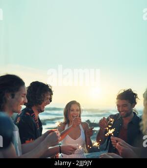 des amis avec des amateurs de sparklers fêtent le nouvel an sur la plage au coucher du soleil Banque D'Images