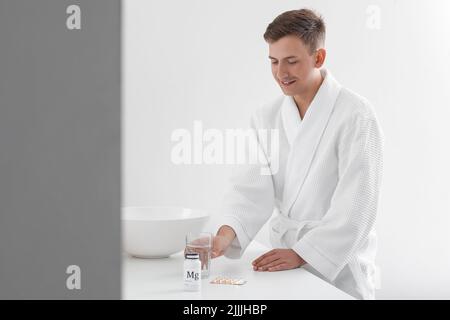 Jeune homme avec un verre d'eau et des pilules dans la salle de bains Banque D'Images