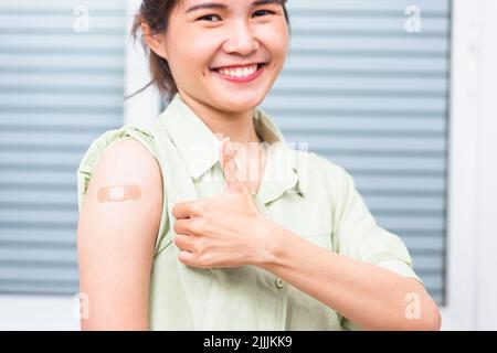 Jeune femme asiatique montrant le pouce gestante vers le haut ou comme et son bras avec bande de plâtre aide après le coronavirus Covid-19 injection sur l'épaule, coron Banque D'Images