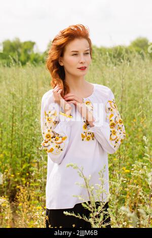 Une jeune femme aux cheveux rouges, belle, dans une chemise ukrainienne brodée marche dans le champ Banque D'Images