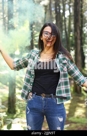 Jeune femme dans un photoshoot levant la main tenant une bombe jaune de fumée dans la forêt souriant au Costa Rica Banque D'Images