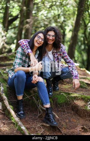 Jeune couple latin assis dans la forêt souriant regardant caméra avec sa main sur son épaule au Costa Rica Banque D'Images