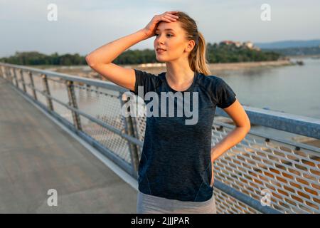 YYoung souriante femme en forme se reposant après un entraînement actif de fitness en plein air dans la ville Banque D'Images
