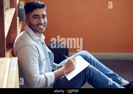 Mon histoire de réussite commence ici. Un jeune homme prend des notes dans une bibliothèque à l'université. Banque D'Images