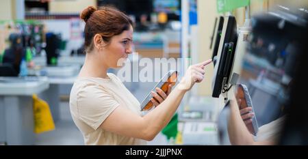 Une femme frustrée utilise un comptoir de caisse libre-service. La fille ne comprend pas comment acheter indépendamment des provisions dans le supermarché sans un vendeur Banque D'Images