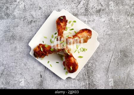 Pilons de poulet cuits au four avec du riz sur une assiette carrée blanche sur fond sombre.Vue de dessus, plan d'appartement Banque D'Images