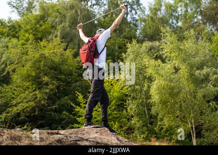 Jeune randonneur avec sac à dos et bâtons de randonnée debout sur le bord de la falaise et regardant les montagnes en été en plein air. Banque D'Images