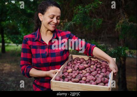 Charmante femme, ouvrier agricole biologique souriant sourire en portant une caisse en bois avec des pots fraîchement récoltés Banque D'Images