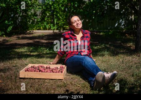 Agréable femme fermier repose sur l'herbe dans une maison de campagne arrière-cour après la récolte de pommes de terre fraîches biologiques Banque D'Images