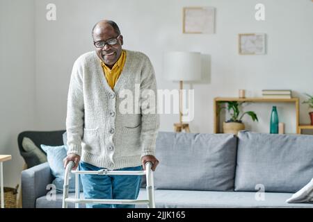 Portrait d'un homme africain âgé avec un handicap souriant à la caméra tout en apprenant à marcher avec un marcheur dans la salle Banque D'Images
