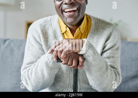Gros plan sur un homme africain de haut niveau qui se penche sur son bâton assis sur un canapé et souriant Banque D'Images