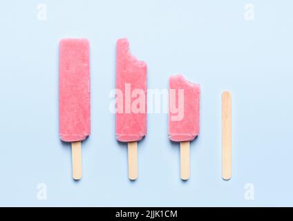Crème glacée à la popsicle rose sur bâton de bois consommation cycle de vie sur fond bleu vue de dessus plat Banque D'Images