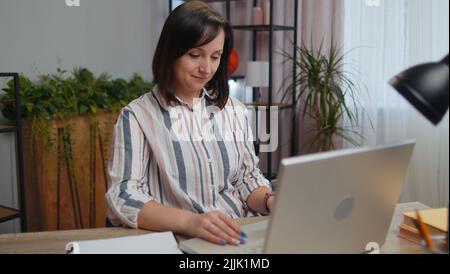 Jeune femme d'affaires freelance à la salle de bureau à domicile, s'assoit au bureau, ouvre l'ordinateur portable. Une jeune fille élève travaille sur un ordinateur portable, envoie des messages, fait des achats en ligne, étudie, e-learning, travail à distance Banque D'Images