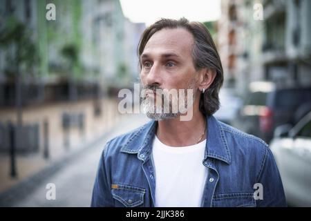 Homme d'âge moyen et mature qui connaît une gueule de bois exténuée émotionnellement et qui a l'air en colère ou frustré. L'homme de crise d'âge moyen ressemble à un alcoolique debout à l'extérieur de fond urbain de ville. Concept de psychologie. Banque D'Images