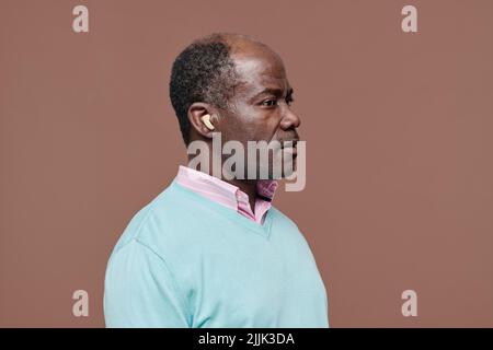Vue latérale d'un homme africain âgé avec une prothèse auditive dans son oreille isolée sur fond beige Banque D'Images