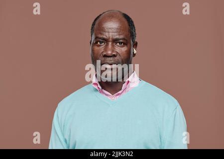 Portrait d'un homme africain âgé avec surdité en chemise bleue regardant l'appareil photo sur fond beige Banque D'Images