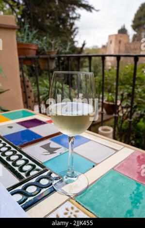 Verre de vin blanc sec espagnol servi sur la terrasse extérieure avec vue sur les murs rouges de la forteresse andalouse médiévale Alhambra à Grenade, Espagne Banque D'Images