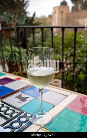 Verre de vin blanc sec espagnol servi sur la terrasse extérieure avec vue sur les murs rouges de la forteresse andalouse médiévale Alhambra à Grenade, Espagne Banque D'Images