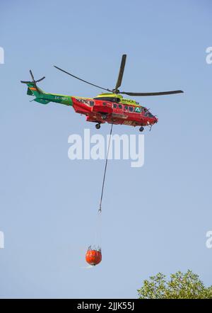 Hélicoptère de l'INFOCA transportant un seau d'eau pour descendre sur un feu de forêt, Mijas, Espagne. Banque D'Images