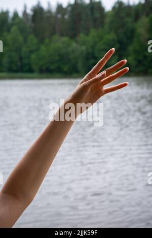 Gros plan de la main femelle dans la manche bleue relevée sur le ciel bleu et le fond des nuages. Les mains des femmes atteignent le ciel. Les gens, l'enfance, les gestes et Banque D'Images