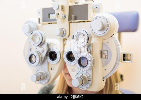 Un ophtalmologiste mâle vérifie la vue d'une jeune fille à l'aide d'un phoroptère. Traitement de la vision. Banque D'Images