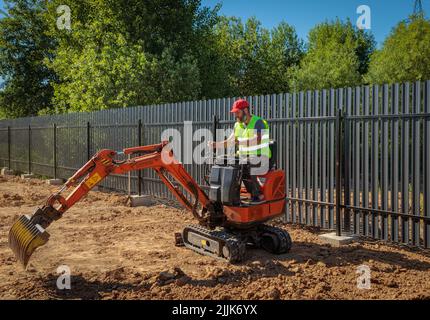 Un homme sur une mini-pelle permet de nivrir un morceau de terre et de détacher le sol Banque D'Images