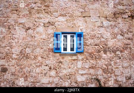 Une fenêtre avec des panneaux blancs et des lamelles en bois bleu dans un vieux mur rustique Banque D'Images