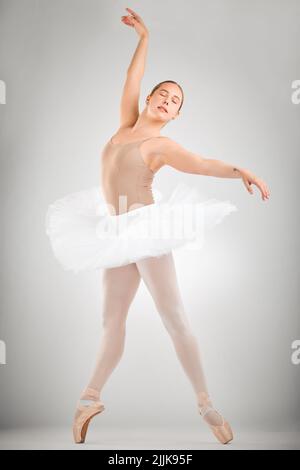 Mettre la FORME dans la performance. Prise de vue en longueur d'une jeune danseuse de ballet attirante en studio sur fond gris. Banque D'Images