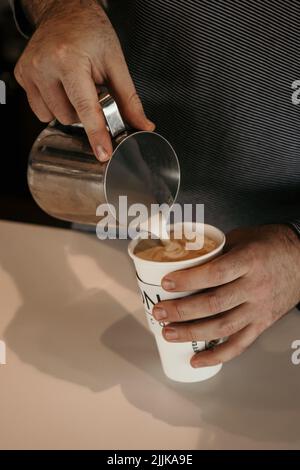 Les mains du barista ajoutent du lait pour préparer un cappuccino Banque D'Images