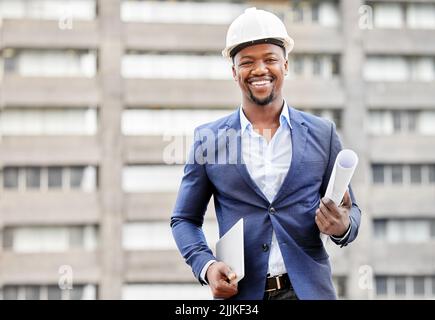 Construction en cours. Portrait rogné d'un jeune homme beau tenant des plans et une tablette debout sur un chantier de construction. Banque D'Images