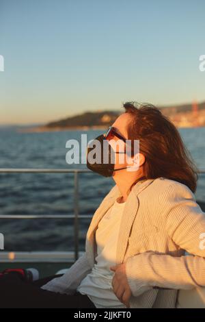 Une jeune femme avec un masque médical et des lunettes de soleil sur un bateau de banlieue Banque D'Images