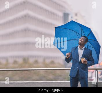 C'est vraiment déversant. Un jeune homme d'affaires tenant un parapluie dans la pluie contre un fond de ville. Banque D'Images