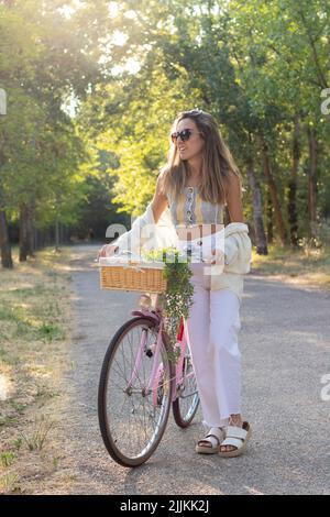 Vue verticale de la jeune femme regardant à côté sur un vélo rétro rose entouré par la nature au printemps Banque D'Images