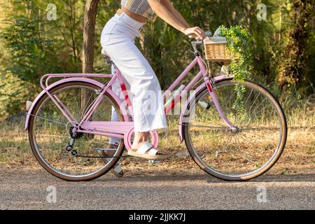 Vue latérale d'une jeune femme méconnaissable sur un vélo rose vintage avec fond naturel sur un pantalon de type while Banque D'Images