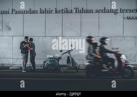 La belle photo de deux jeunes hommes à côté d'une vespa moto et d'une famille est de conduire une moto qui accélère en face d'eux Banque D'Images