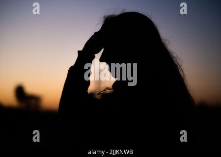 Foyer sélectif de la silhouette d'une fille en profil, souriant et tenant sa tête avec le coucher du soleil en arrière-plan Banque D'Images